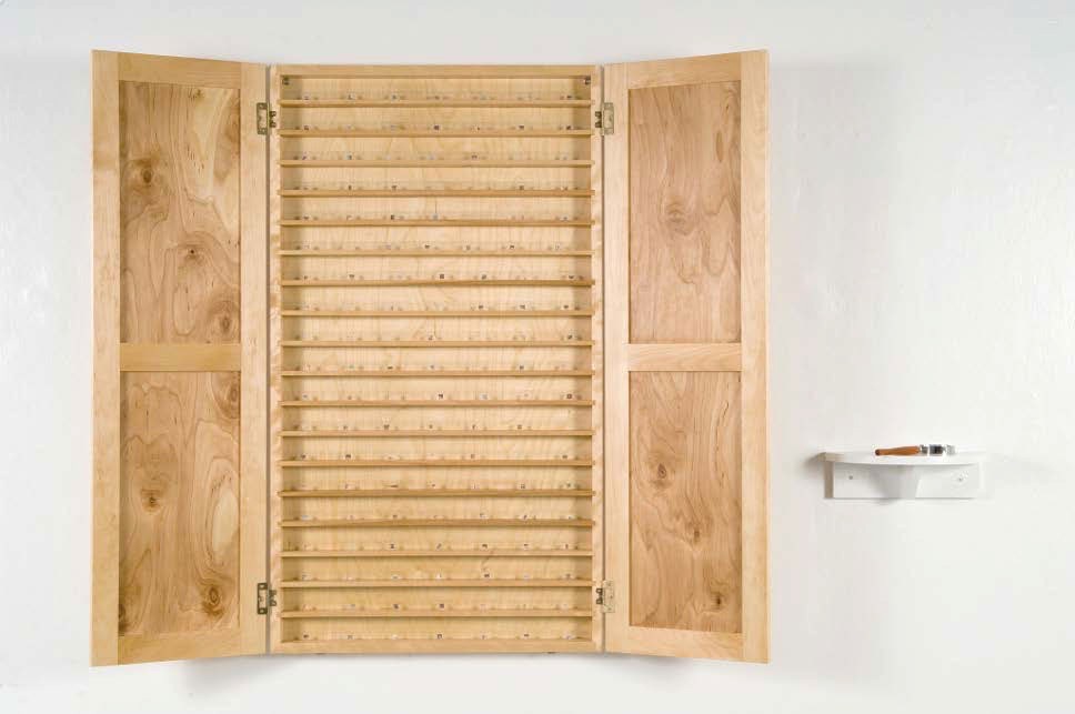 A pale wooden cupboard with its doors open, the interior fitted with rows of narrow slots, and a small shelf mounted beside it.