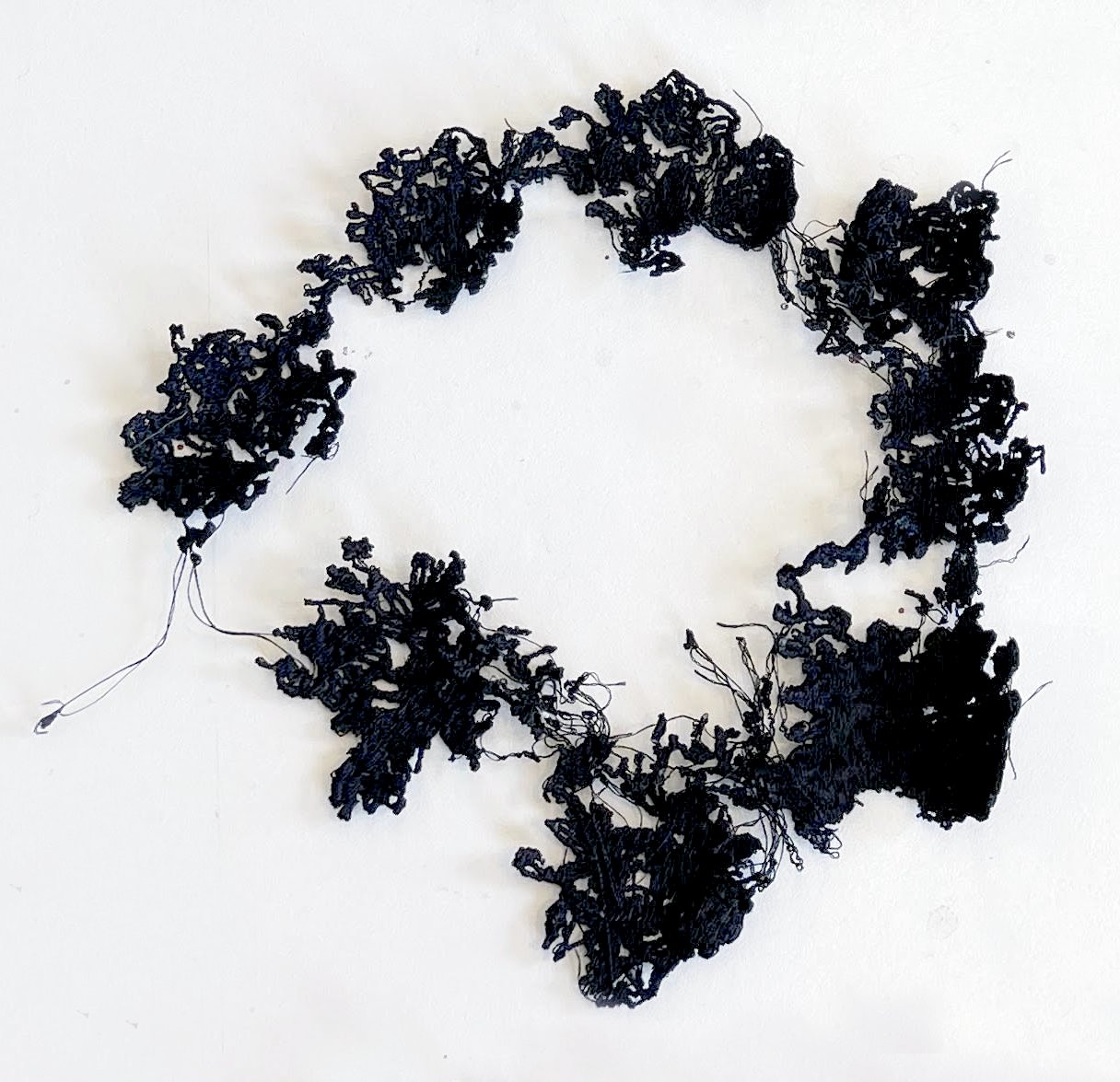A loose ring of black machine-stitched lace in dense clusters, like blossoms joined by fine threads, on a white ground.