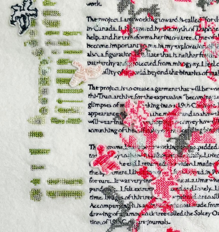 Close view of the embroidered email: lines of black stitched text crossed by pink cross-stitch blossoms, felt appliqué flowers, and green stitched bars in the margin.