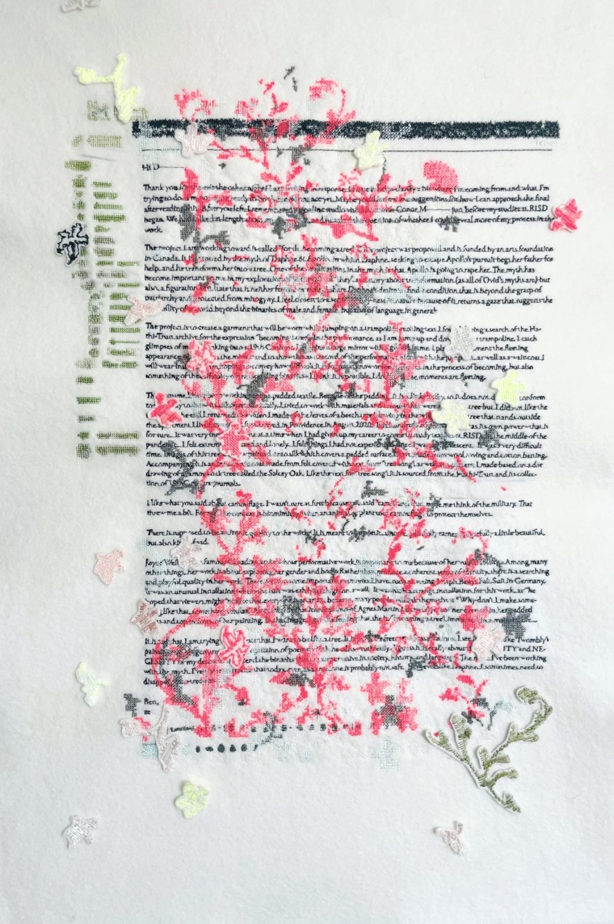 An embroidered email on white fabric: lines of dark machine-stitched text overlaid with pink stitched blossoms and green appliqué.