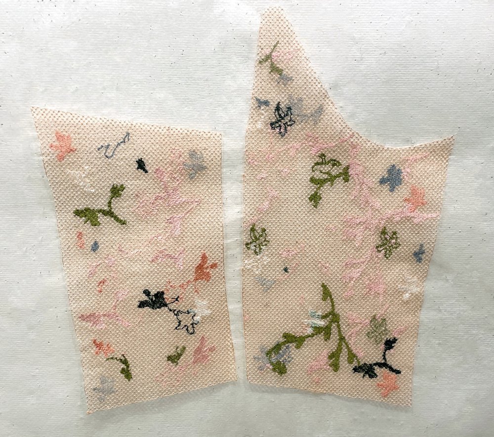 Two pieces of pale peach tulle, cut as sleeve and bodice pattern pieces, embroidered with small pink, green, black and blue blossoms.
