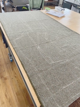 Tweed laid on the cutting table with pattern components chalked onto it.
