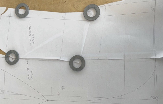 A full-scale paper pattern draft held flat with weights.