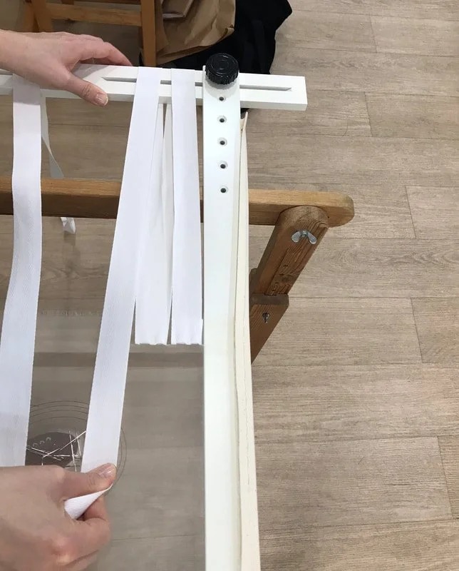 Cloth being laced into a wooden slate frame with cotton tape.