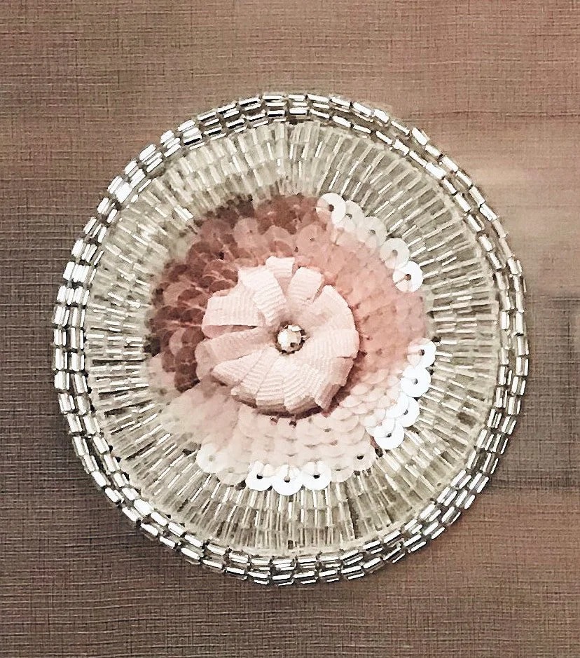 A rosette of pink sequins and ribbon ringed with silver bugle beads.