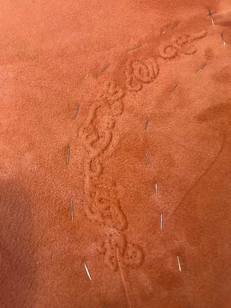 A chain-stitched scroll on rust suede, pinned.
