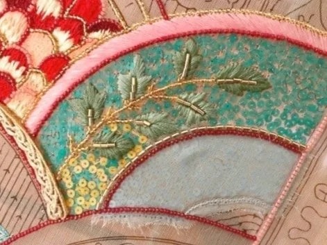 Detail of the sampler: a fan of green leaves and gold beads on a turquoise ground.