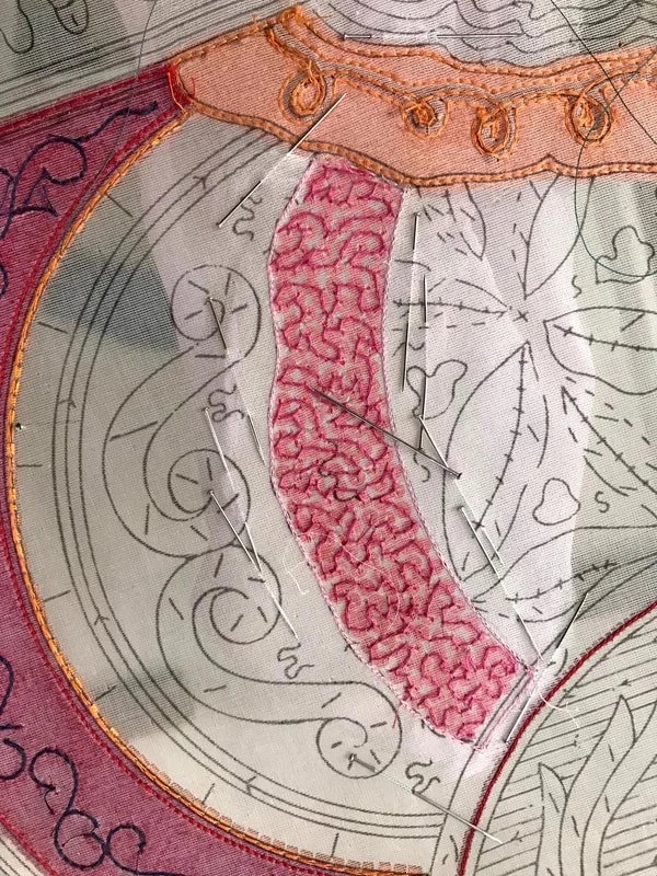 Detail of the sampler: vermicelli filling in pink beside pencilled outlines, with needles parked in the cloth.