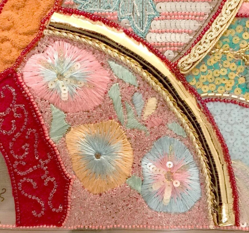 Detail of the sampler: pastel flowers worked in sequins and thread beside a gold braid.