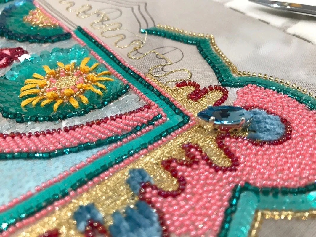 Detail: a sunburst in yellow thread set in beaded pink and turquoise bands, with a blue stone.