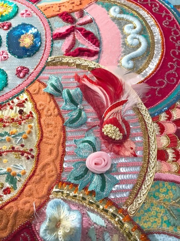 Detail: a red feathered motif and a small pink ribbon rose.