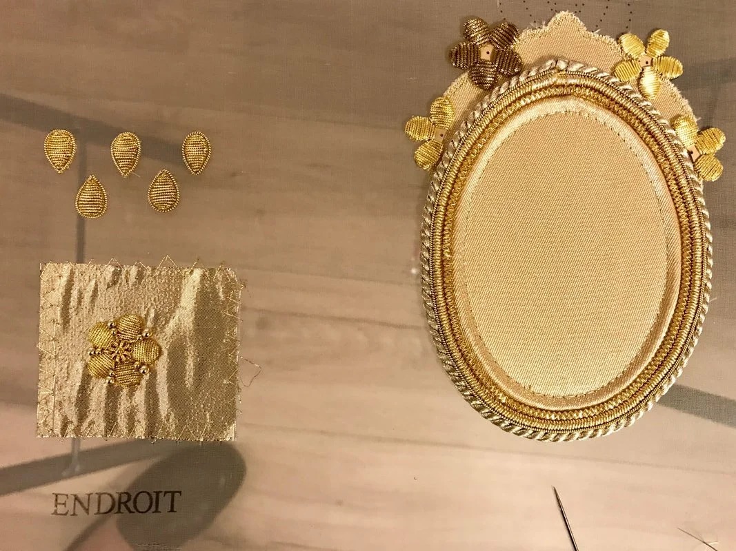 Goldwork: an oval frame of couched cord with cannetille flowers, and a square sample marked ENDROIT.
