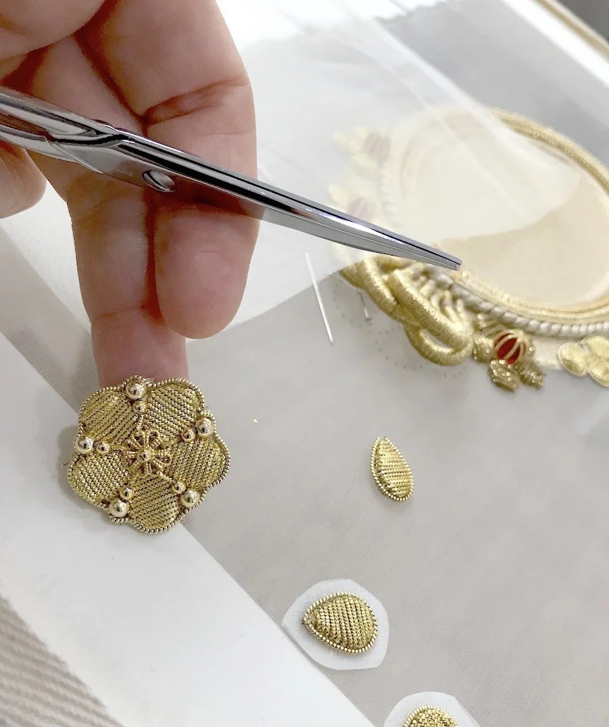 A goldwork flower held between finger and scissors.
