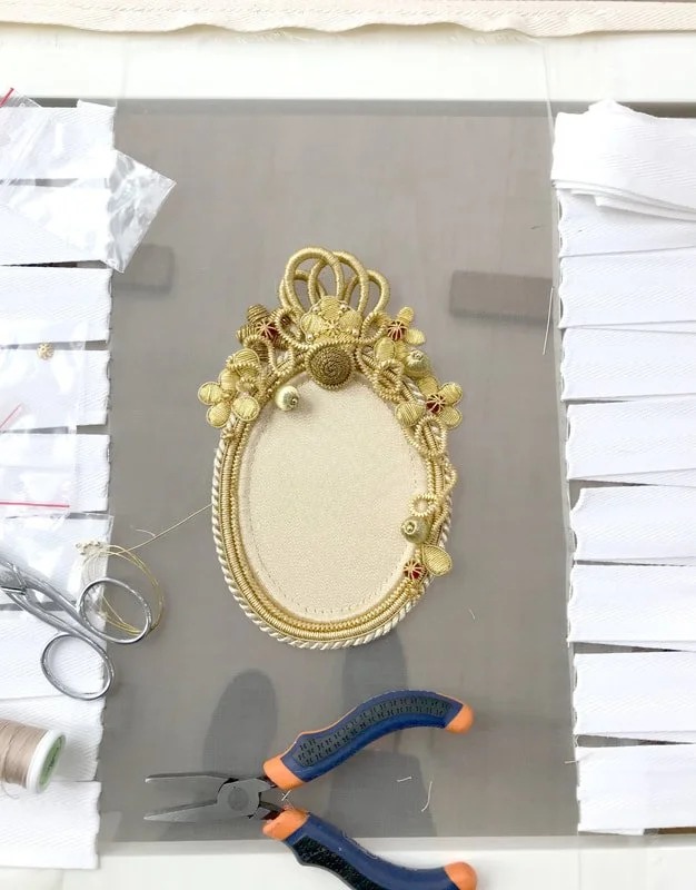 The goldwork oval on the frame, with scissors and pliers beside it.