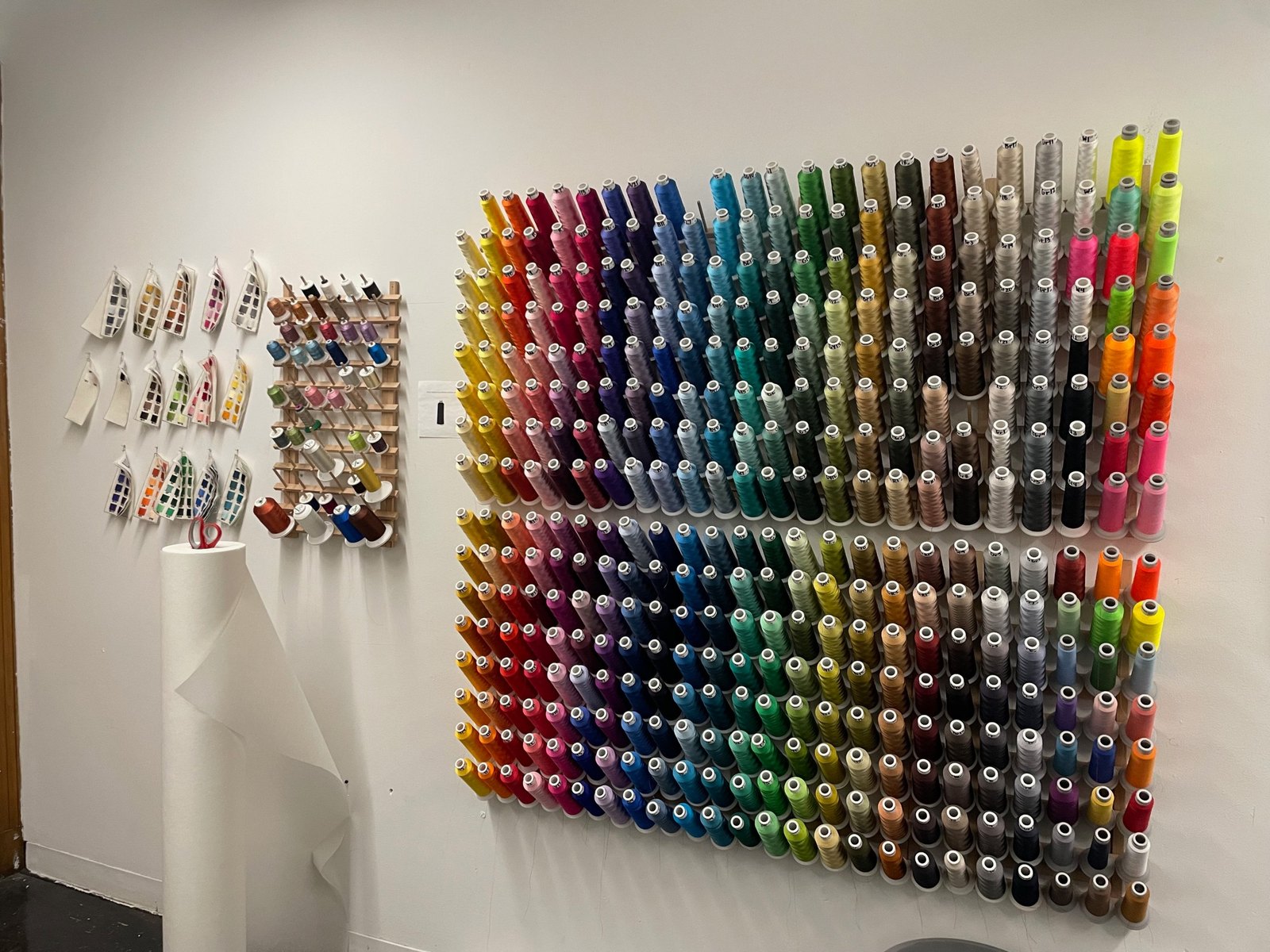 A wall of embroidery thread cones in rows graded by colour, with small stitched colour samplers beside it.